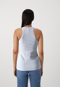Top senza maniche a costine blu chiaro con scollo alto, forma aderente e texture liscia, abbinato a jeans in denim blu medio.
