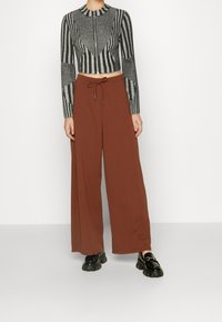 Maglione a righe grigie e nere, corto, con maniche lunghe e colletto alto, abbinato a pantaloni marroni a gamba larga e scarpe nere chunky.