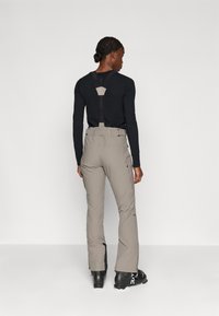 Pantaloni de schi din țesătură gri deschis cu accente negre, dotati cu bretele ajustabile, un buzunar cu fermoar și un design cu picior evazat.
