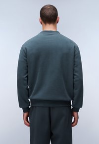Tmavě zelená mikina vyrobená z měkké tkaniny, s dlouhými rukávy, žebrovanými manžetami a lemem, a kulatým výstřihem. Ukázaný zadní pohled.