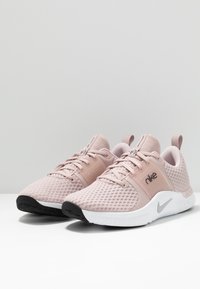 Ljust rosa träningssneakers med ovandel i mesh, tonade snören och en vit mellansula. Har en svart gummisula och en silverfärgad Nike-logotyp.