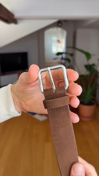 Brauner Wildledergürtel mit rechteckiger silberner Metallschnalle, glatter Textur und sauberer Naht entlang der Kanten.