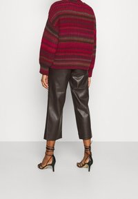 Chunky stickad tröja i röd och brun rand, kombinerad med bruna byxor i faux läder med vida ben och svarta remsandaler med hög klack.