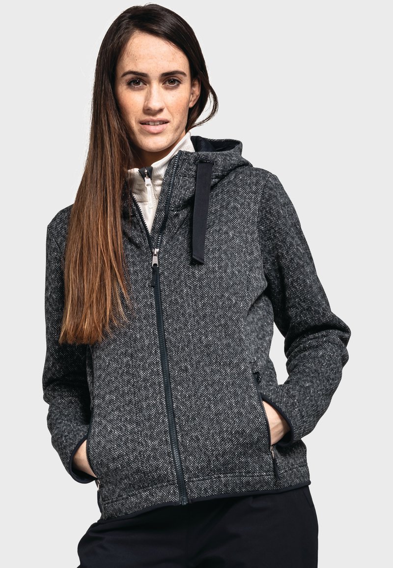 Chaqueta gris texturizada con cremallera frontal, capucha y bolsillos laterales. Presenta un patrón geométrico y cremallera negra contrastante con acentos.