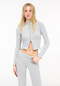 Harmaa uurrettu vetoketjullinen croptop pitkillä hihoilla, yhdistettynä samaa materiaalia oleviin korkeavyötäröisiin housuihin, jotka ovat pehmeää ja teksturoitua kangasta.
