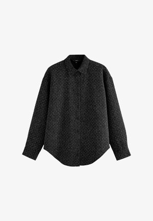 Musta napillinen paita, jossa on teksturoitu kangas ja pilkullinen kuvio. Pitkät hihat klassisella kauluksella ja kaareva helma.