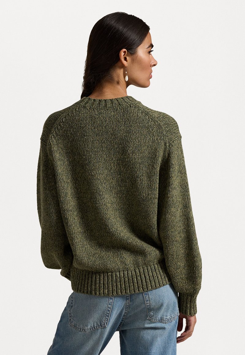 Groene gebreide trui met structuur, een ronde hals, verlaagde schouders en een ribgebreide zoom, gecombineerd met lichtblauwe jeans.