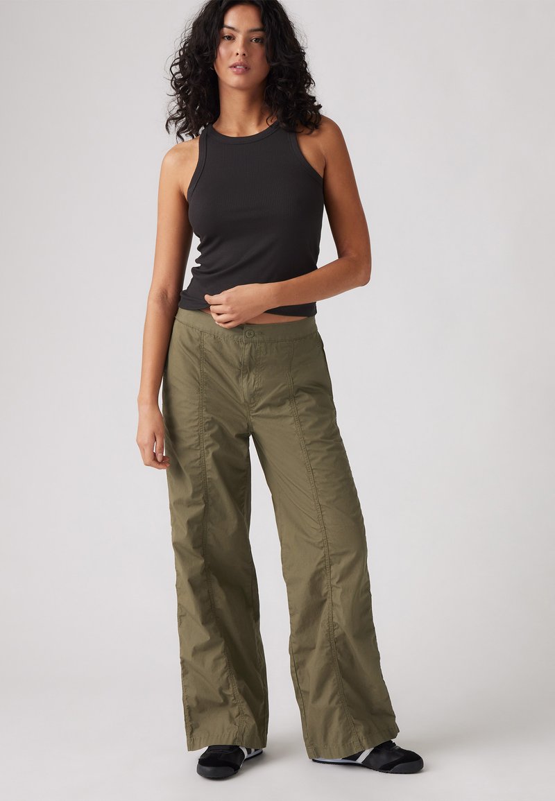 Débardeur noir à côtes associé à un pantalon olive à jambes larges en tissu léger et lisse ; design minimaliste sans motifs visibles.