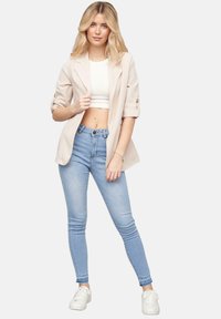 Beige blazer met opgerolde mouwen, witte crop top, lichtblauwe skinny jeans en witte sneakers. Minimalistisch ontwerp, getailleerde silhouette.