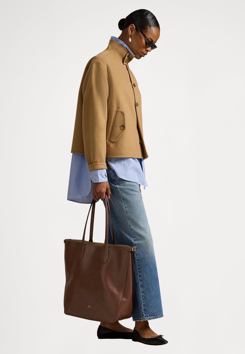 Braune Jacke aus Wollmischung mit vorderen Knöpfen, hellblaues Hemd und Jeans mit weitem Bein. Braune Ledertasche, schwarze Ballerinas, minimalistisches Design.