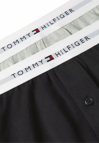 Fasce in vita per biancheria intima con il logo Tommy Hilfiger, una in tessuto grigio e una in tessuto nero, mostrate da vicino con dettagli dei bottoni.
