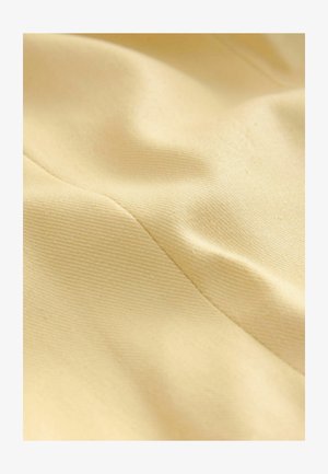 Tasapinnaline puuvillane kangas heledas kollases, millel on tekstuuriga pind, peen sära ja nähtavad õmblusjooned. Sile ja pehme tekstuur.