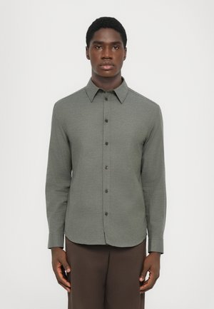 Long-sleeve, collared shirt in textured olive green fabric with a buttoned front and brown buttons. Tailored fit with curved hem.