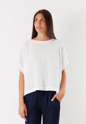 Top bianco in lino, morbido e largo, con maniche ampie, scollo rotondo e orlo dritto, abbinato a pantaloni navy con cordoncino.