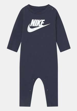 Granatowy kombinezon z długim rękawem wykonany z miękkiego materiału, z wyraźnym białym logo Nike oraz zatrzaskami na ramieniu i u dołu.