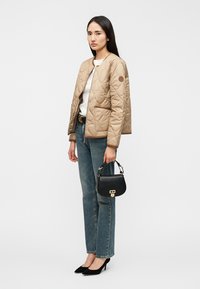 Μπεζ μπουφάν με ραμμένο σχέδιο, στρογγυλή λαιμόκοψη και φερμουάρ, συνδυασμένο με λευκή μπλούζα, μπλε τζιν, μαύρη τσάντα και μαύρες ψηλοτάκουνες γόβες.