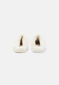 White, plush slippers with a soft faux fur upper and a flat sole. The interior is lined for comfort, featuring an open-back design for easy wear.