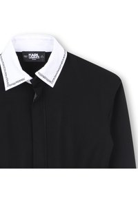 Black shirt with a white collar featuring a dotted pattern along the edges. Includes a front button closure and soft fabric texture.