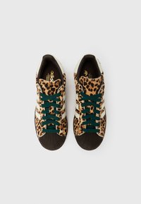Par superg Adidas z leopardjim vzorcem, temno zelenimi vezalkami, črnimi kapicami na prstih in belimi ikonastimi tremi črtami, pogled od zgoraj.