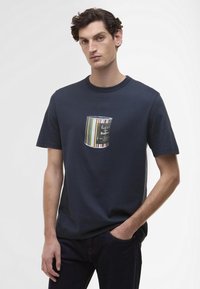 T-shirt de algodão azul-marinho com um design de bolso gráfico que se assemelha a uma lata de tinta com riscas multicoloridas e texto impresso.