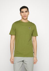 Oliven grøn T-shirt med korte ærmer lavet af bomuld. Har et sort Puma-logo på brystet og en klassisk rund halsudskæring. Simpelt design.