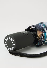 Parapluie compact noir avec une canopée à motifs bleus et multicolores élaborés, doté d'une poignée ronde noire avec une marque blanche.