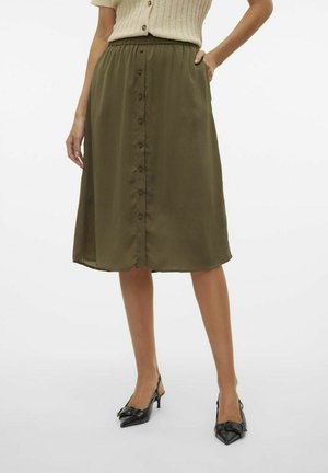 Jupe midi olive en tissu lisse, avec une taille froncée, des boutons à l'avant et un drapé fluide. Associée à des chaussures à talons noires.