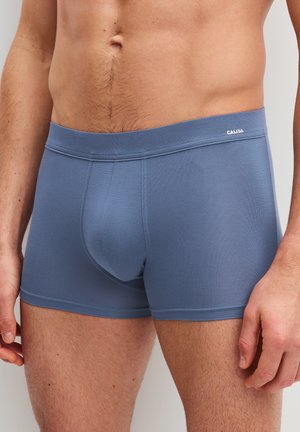 Man draagt nauwsluitende blauwe Calida boxershorts, toont torso en bovenbenen tegen een effen achtergrond.