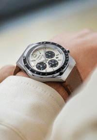 Silberner Edelstahlarmbanduhr mit cremefarbenem Zifferblatt, schwarzen Unterzifferblättern und schwarzem Lünette. Verfügt über ein braunes Lederband und Chronographenfunktion.