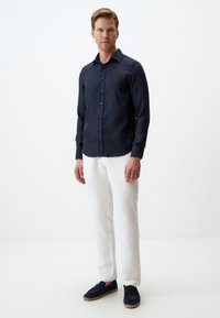 Marineblauw overhemd met knopen en een gladde textuur, gecombineerd met witte linnen broek. Het schoeisel is marineblauw en heeft een touwaccent.