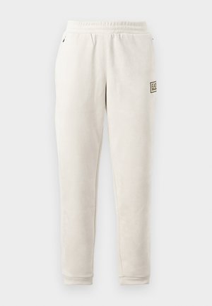 Calças jogger beige em tecido suave com um cós elástico. Apresentam bolsos laterais e um pequeno emblema na perna esquerda.