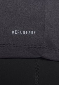 Tissu athlétique gris foncé avec l'inscription "AEROREADY" en gris clair au-dessus d'une couture et tissu noir en dessous.