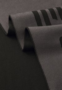 Tissu tricoté en gris foncé et noir, présentant une texture lisse avec des couches superposées et des rayures horizontales.