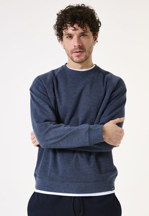 Donkerblauwe crewneck sweatshirt met lange mouwen, subtiele textuur, ribgebreide manchetten en zoom, gelaagd over een wit T-shirt.