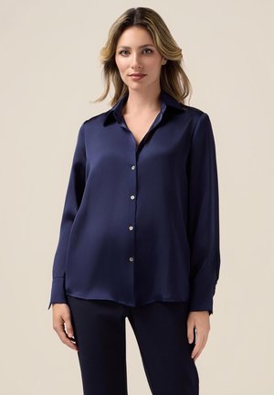 Navyblaue Satinbluse mit langen Ärmeln, einem Kragen und einer Knopfleiste. Sie hat eine glatte Textur und einen sanft abgerundeten Saum.