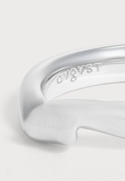 Gros plan d'une bague en argent lisse avec le mot "avgvst" gravé à l'intérieur de l'anneau.