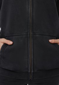 Μαύρο φούτερ με φερμουάρ, με λεία υφή, μπροστινές τσέ�πες και χρυσό φερμουάρ. Οι ριμπ μανσέτες και το τελείωμα προσθέτουν επιπλέον λεπτομέρεια.