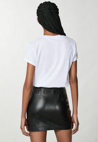 T-shirt bianco in cotone con maniche arrotolate abbinato a una mini gonna nera in pelle. La gonna ha una texture liscia e una silhouette aderente.