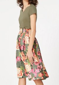 Olijfgroene, aansluitende top gecombineerd met een knielange rok met een bloemenpatroon in roze, oranje en groentinten, met een elastische taille.