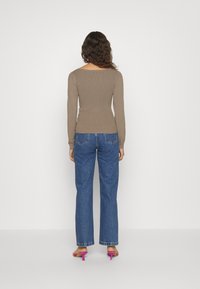 Braunes, geripptes Langarm-Oberteil mit quadratischem Ausschnitt, kombiniert mit hoch taillierten blauen Jeans mit Schlag und rosa Sandalen mit Absatz.