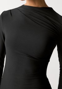 Robe noire à manches longues en matière lisse, présentant un design drapé sur l'épaule et une silhouette ajustée.