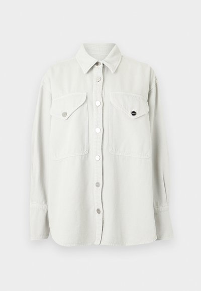 Λευκό πουκάμισο με μακριά μανίκια, γιακά και δύο εμπρόσθιες τσέπες με μεταλλικά κουμπιά τύπου σούστα