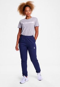 Szary bawełniany t-shirt z logo "Hummel", w zestawie z granatowymi spodnie dresowymi z elastycznym pasem i detalem logo, uzupełnione białymi trampkami.