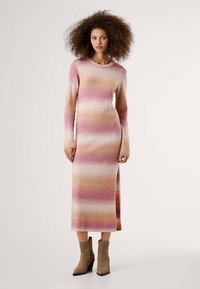 Vestido de malha em riscas degradê de rosa, bege e creme; mangas compridas, decote redondo, comprimento médio com fenda lateral; usado com botas de tornozelo taupe.