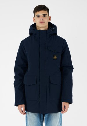 Parka blu navy con cappuccio staccabile, chiusura frontale con zip, multiple tasche con flap e patch con logo sul petto. Tessuto dalla texture liscia.