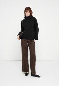 Pull à col roulé noir à manches longues, associé à un pantalon large marron et des ballerines noires, accessoirisé avec un petit sac à main sombre.
