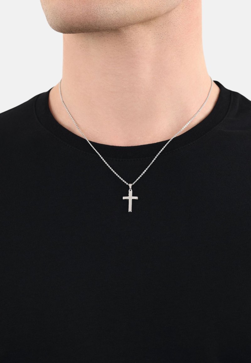 Silberner Kreuzanhänger an einer schwarzen Kette, getragen auf einem schwarzen T-Shirt. Der Anhänger ist einfach, flach und hat eine polierte Oberfläche.