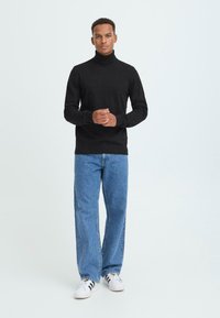 Schwarzer Rollkragenpullover, gestrickter Stoff, figurbetont. Kombiniert mit hellblauen, geraden Jeans und weißen Sneakers mit schwarzen Streifen.