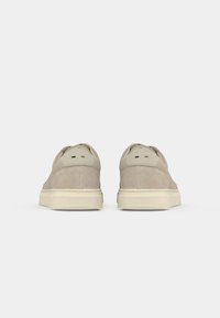 Beige suede casual sneakers shown from the back with cream-colored soles and small black, white, and tan stitched details on heel tabs.