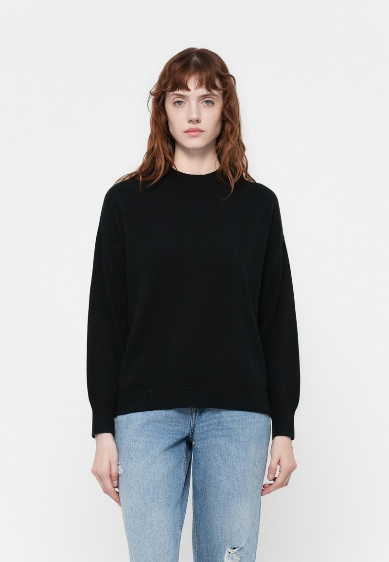 Pull noir à col haut, à coupe ample et épaules tombantes, associé à un jean clair déchiré.